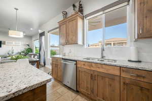 Kitchen with light stone counters, dishwasher, backsplash, open floor plan, and light tile patterned floors
