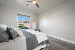 Bedroom with wood finished floors, a ceiling fan, a raised ceiling, and crown molding
