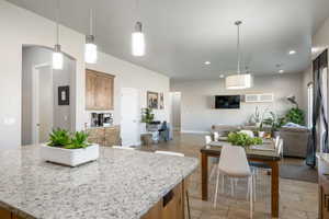 Kitchen with pendant lighting, light stone countertops, brown cabinets, open floor plan, and a center island