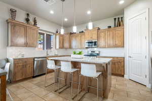 Kitchen with a breakfast bar area, pendant lighting, a kitchen island, stainless steel appliances, and light stone counters