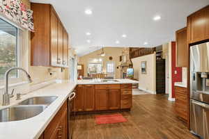 Kitchen with a peninsula, brown cabinetry, appliances with stainless steel finishes, dark wood-type flooring, and vaulted ceiling