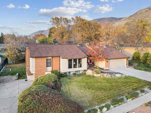 Single story home featuring a mountain view, a shingled roof, a front yard, driveway, and brick siding