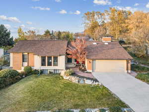 View of front of home with a shingled roof, a front yard, driveway, an attached garage, and brick siding