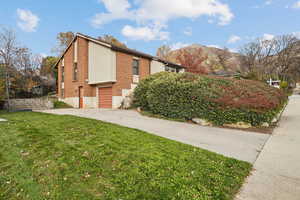 View of side of home featuring brick siding, a lawn, a mountain view, a garage, and driveway