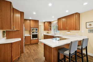 Kitchen with brown cabinets, open shelves, dark wood-style flooring, a breakfast bar area, and recessed lighting