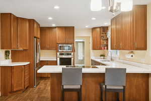 Kitchen featuring open shelves, brown cabinetry, stainless steel appliances, a peninsula, and a breakfast bar