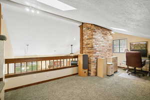 Office space featuring a skylight, vaulted ceiling, carpet flooring, and a textured ceiling