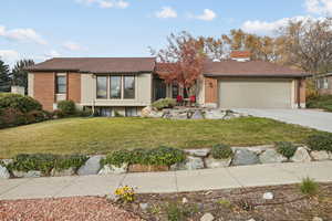 View of front of property with brick siding, a front lawn, a chimney, concrete driveway, and roof with shingles