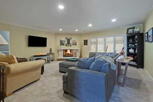 Living area featuring crown molding, a lit fireplace, light carpet, and recessed lighting