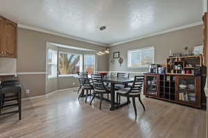 Dining room featuring a textured ceiling, healthy amount of natural light, light wood-type flooring, and ornamental molding