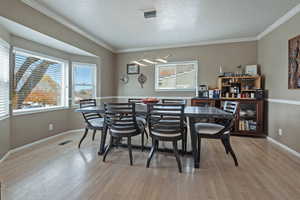 Dining area with ornamental molding, light wood finished floors, and a textured ceiling