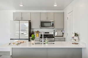 Kitchen with gray cabinets, appliances with stainless steel finishes, light stone countertops, light wood finished floors, and a textured ceiling