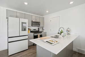 Kitchen featuring gray cabinetry, appliances with stainless steel finishes, dark wood-style flooring, a peninsula, and light stone counters