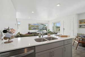Kitchen with open floor plan, stainless steel dishwasher, gray cabinets, light stone counters, and wood finished floors