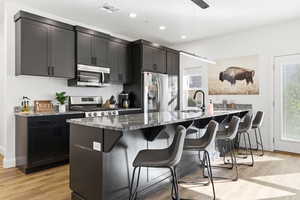 Kitchen featuring dark stone countertops, light wood finished floors, stainless steel appliances, a breakfast bar, and recessed lighting