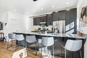 Kitchen with light stone counters, a breakfast bar area, stainless steel appliances, recessed lighting, and light wood-style flooring