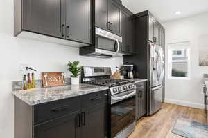 Kitchen with stainless steel appliances, light wood finished floors, light stone counters, and dark cabinets