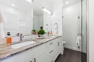 Bathroom with a shower stall, double vanity, dark tile patterned flooring, and recessed lighting
