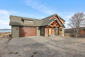 View of front facade featuring a shingled roof, driveway, a water view, and a garage