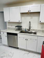 Kitchen with light marble finish floors, stainless steel dishwasher, white cabinets, and light stone countertops
