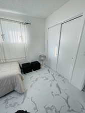Bedroom with light marble finish flooring, a textured ceiling, and a closet