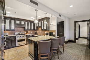 Kitchen featuring recessed lighting, high end appliances, a breakfast bar, light stone countertops, and glass insert cabinets