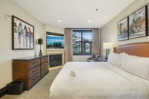 Bedroom with a glass covered fireplace, light colored carpet, and recessed lighting