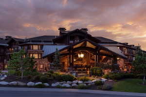 Back of house at dusk with a standing seam roof, a metal roof, stone siding, a chimney, and a balcony