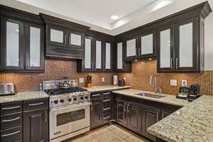 Kitchen with premium stove, glass insert cabinets, light stone counters, decorative backsplash, and light tile patterned floors