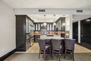 Kitchen with a kitchen breakfast bar, light stone countertops, glass insert cabinets, backsplash, and hanging light fixtures