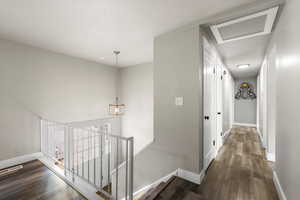 Hallway featuring vinyl flooring, an upstairs landing, attic access, and a chandelier