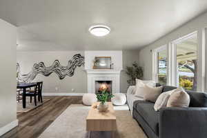 Living room with vinyl floors, a textured ceiling, and a warm lit fireplace
