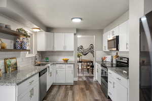 Kitchen featuring appliances with stainless steel finishes, light granite counters, open shelves, and vinyl floors