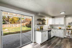 Kitchen with open shelves, light stone counters, a textured ceiling, vinyl floors, and tasteful backsplash