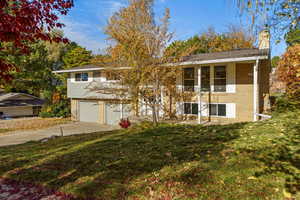 Split entry home featuring brick siding, a front yard, a chimney, driveway, and an attached garage