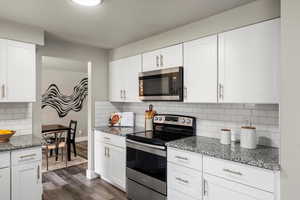 Kitchen with stainless steel appliances, light stone counters, white cabinetry, vinyl flooring, and backsplash