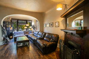 Living room featuring a brick fireplace, dark wood-style flooring