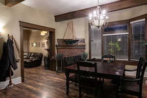 Dining space featuring a fireplace, beam ceiling, dark hardwood/wood-style flooring and an inviting chandelier