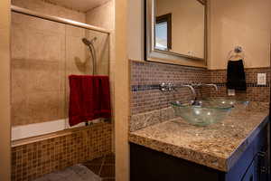 Bathroom featuring tiled shower / bath combo, vanity, tasteful backsplash, and dark tile patterned floors