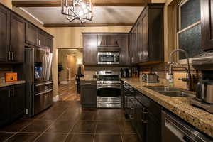 Kitchen with backsplash, dark brown cabinetry, stainless steel appliances, light stone counters, and beamed ceiling
