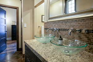 Bathroom with dark tile patterned flooring, vanity, and backsplash