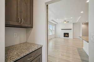 Kitchen featuring dark brown cabinets, a raised ceiling, light stone counters, recessed lighting, and light wood-style floors