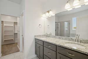 Bathroom with a walk in closet, double vanity, light tile patterned floors, and a stall shower