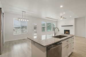 Kitchen featuring a glass covered fireplace, a raised ceiling, dishwasher, light stone countertops, and hanging light fixtures