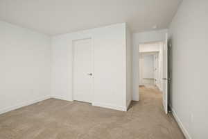 Unfurnished bedroom featuring light carpet and baseboards