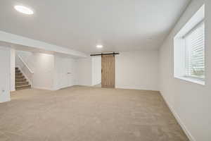 Basement with a barn door, light colored carpet, stairs, and recessed lighting