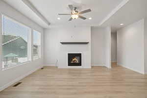 Unfurnished living room featuring a raised ceiling, recessed lighting, a glass covered fireplace, light wood-style flooring, and a ceiling fan