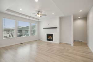 Unfurnished living room with a raised ceiling, recessed lighting, a lit fireplace, ceiling fan, and light wood-style flooring