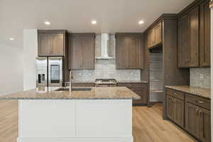 Kitchen with appliances with stainless steel finishes, light stone counters, wall chimney exhaust hood, light wood-type flooring, and recessed lighting