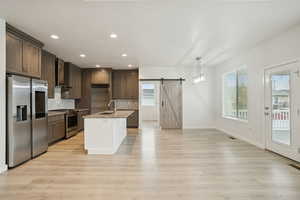 Kitchen featuring a barn door, appliances with stainless steel finishes, recessed lighting, tasteful backsplash, and light stone countertops